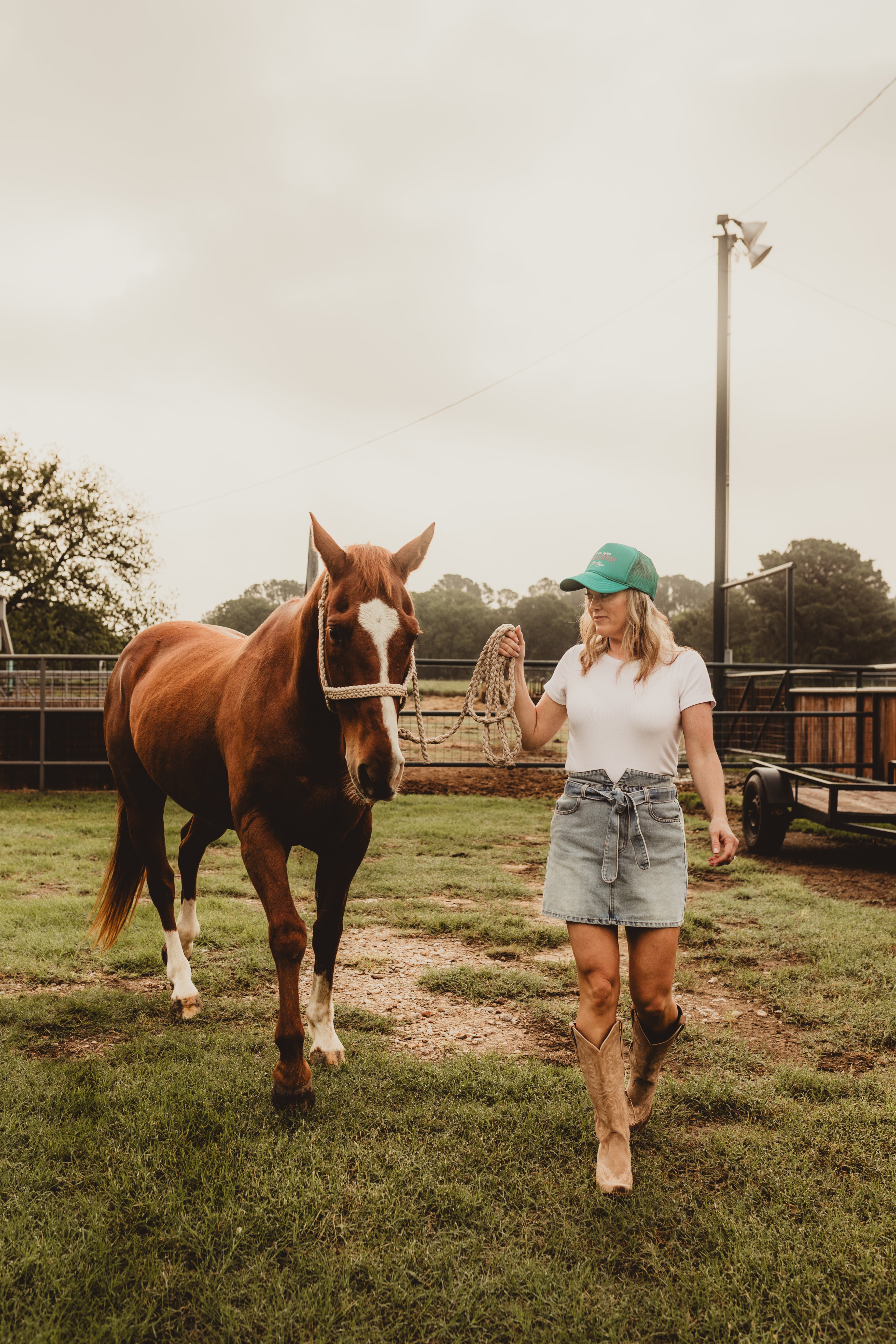 Woman walking a horse on a grassy field with a cloudy sky.